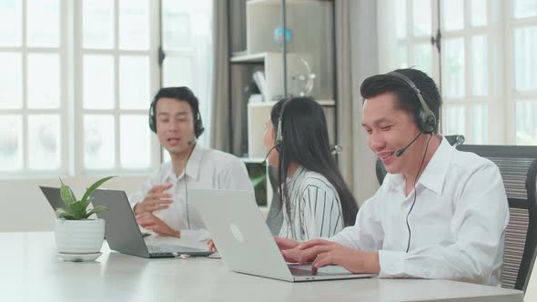 A Man Of Three Asian Call Centre Agents Speaking To Customer While His Colleagues Are Talking