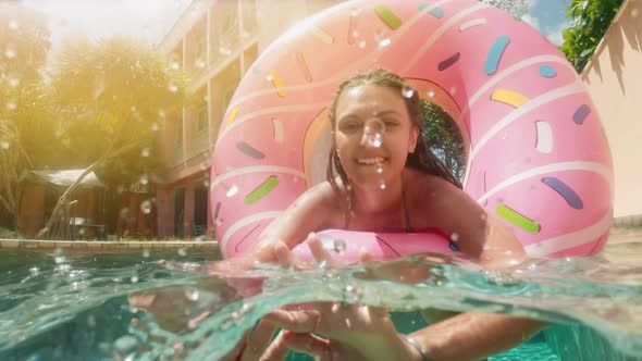 Woman with Sunglasses in Blue Bikini Lying in Inflatable Pink Donut Float in Pool on Sunny Summer