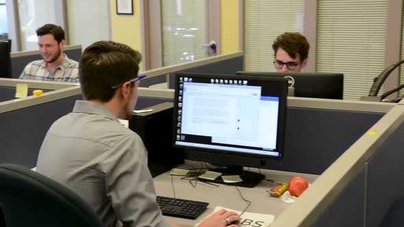 Left panning shot of young professionals working in cubicles on computers