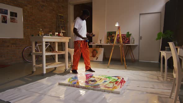 African american male artist pouring paint on canvas at art studio