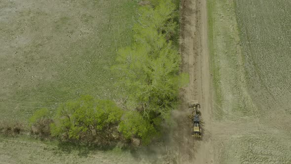 Overhead Road Grader levelling dusty country road next to green tree lane