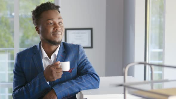 Happy African Businessman Taking Break in Office Drinking Coffee Standing in Window and Daydreaming