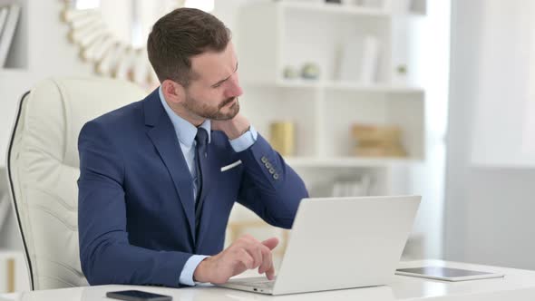 Businessman with Laptop Having Neck Pain in Office 