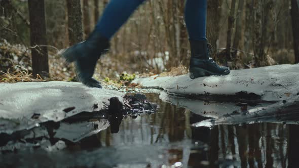 Woman with black high heels boots stepping over small puddle in forest. Camera close to ground