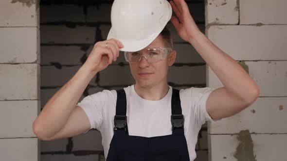 A Male Worker Puts on a White Construction Helmet on a Construction Site
