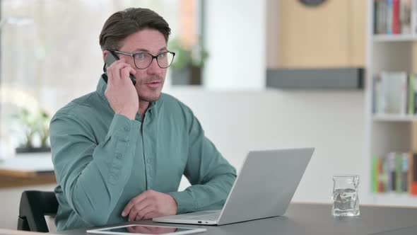 Middle Aged Man Talking on Phone While Working on Laptop