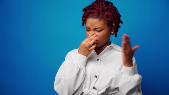 Afro Woman in White Shirt Close Nose Because of a Bad Stinky Smell Blue Background