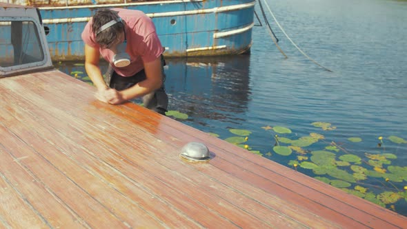 Youth sanding boat cabin roof planks with sandpaper wearing mask