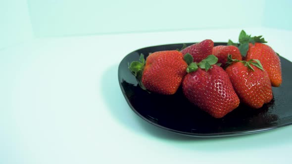 Fresh big red tasty ripe strawberries rotates slowly on a black plate on light blue background, heal