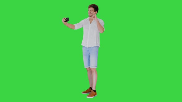 Young Man in Casual White Shirt Taking Selfies on His Phone on a Green Screen, Chroma Key.