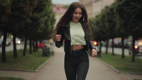A Young Woman is Walking and Listening to Music with Headphones