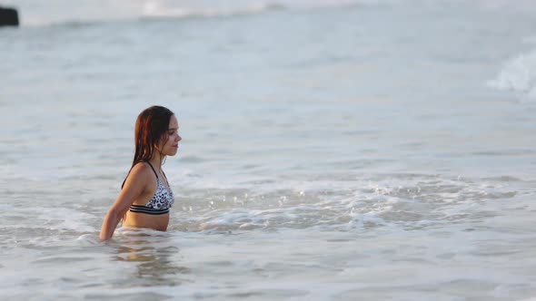 Girl with Wet Hair in a Leopard Swimsuit Splashes Water While Sitting in the Sea