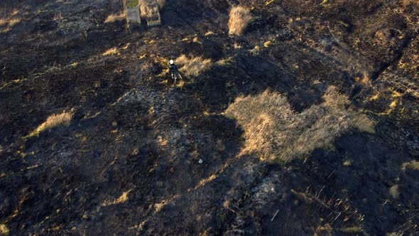 One Firefighters Walk on Black Scorched Earth After Fire and Burning Dry Grass