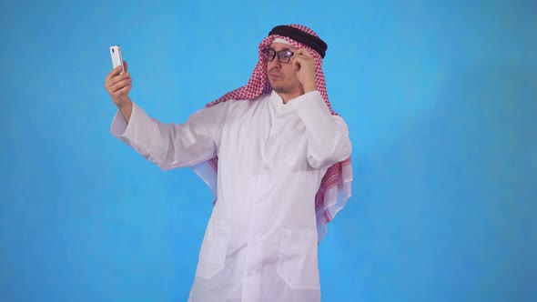 Arab Man Takes a Selfie on the Smartphone Camera on a Blue Background