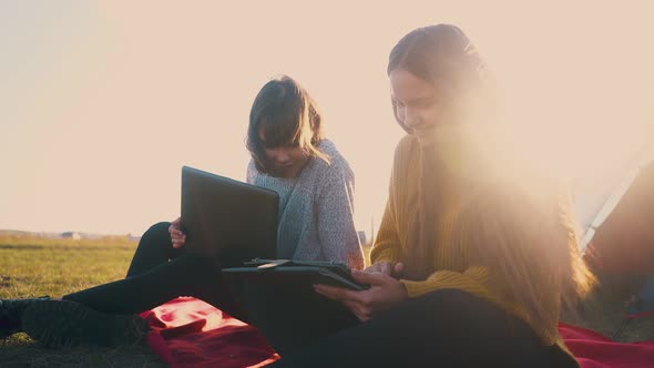 Smiling Women with Tablet and Laptop at Tent Against Sunset