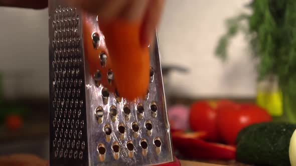 female hands rub carrots on table against background of vegetables and herbs.