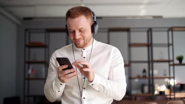 Happy Cheerful Young Man Is Listening Music in Headphone Using Mobile Phone