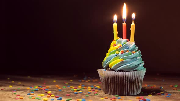 Birthday Cupcake with Blue and Yellow Cream Icing and Lit Candles on a Wooden Table