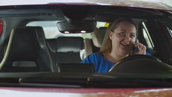 Young Stout Woman Talking on Smartphone and Smiling Sitting in Car Drive Seat