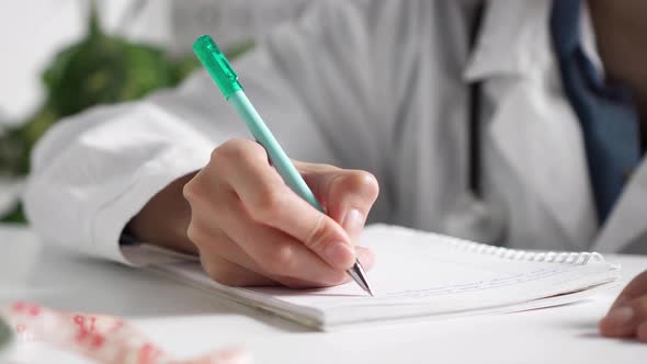 The Hand Writes In The Diary. Records Patient Information A Girl Doctor Sits At A Table In A Medical