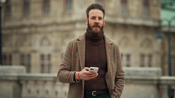 Young Man Walking and Holding a Smartphone Front of Building