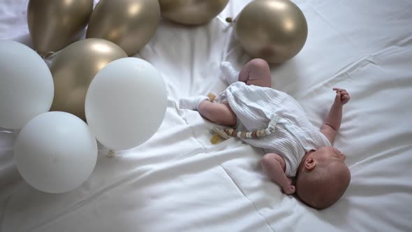 High Angle View Carefree Newborn Baby Lying on White Soft Comfortable Bed with Balloons Around