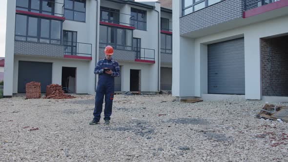 Man Looks on His Black Tablet on Building