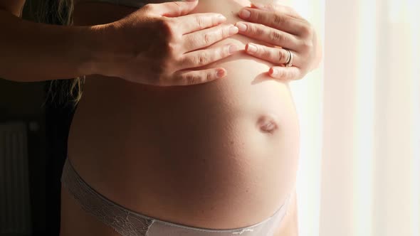 Closeup of Pregnant Woman Standing in Sun Light and Gently Stroking Her Big Belly