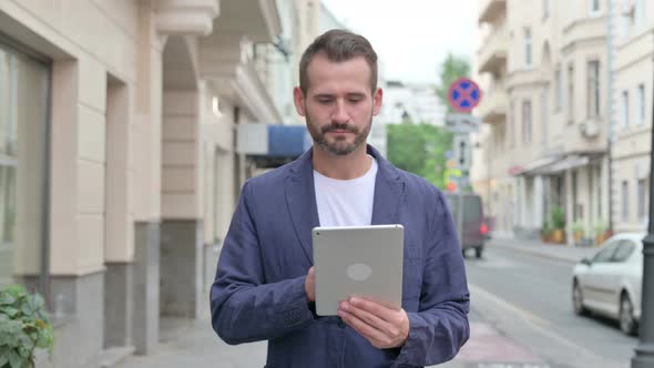 Happy Mature Adult Man Browsing Internet on Tablet While Walking Down the Street