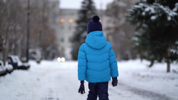 Cute Four Years Old Boy in Blue Winter Clothes Walks in Snowy Street