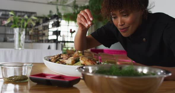 Mixed race female chef preparing a dish and smiling in a kitchen