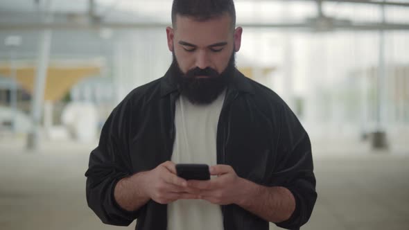 Front View of Young Bearded Man Typing Message on Phone