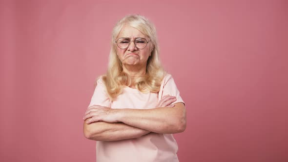 Grumpy Senior Woman Looking at Camera and Gesturing Thumb Up Gesture Pink Studio Background