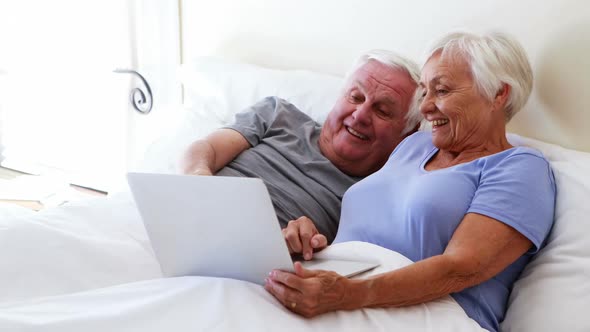 Happy senior couple using laptop on bed