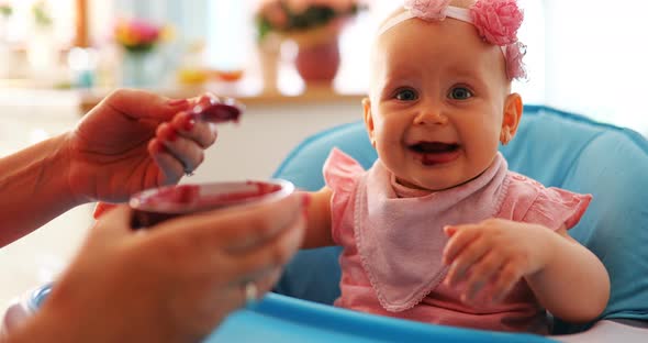 Mother Feeding Baby with Spoon Indoors at Home