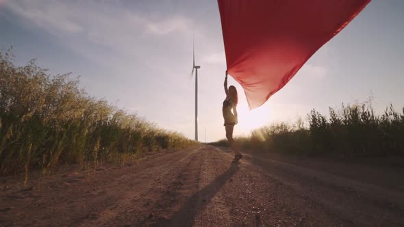 Woman with Pieces of Red Cloth Dance Near the Field with Wind Generators 