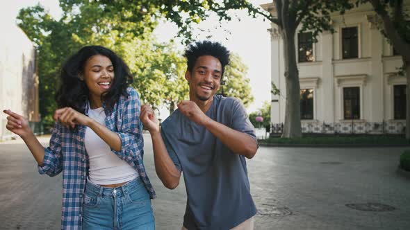 Ethnic Black Male and Female Smiling Dancing Synchronously While Walking By City Square