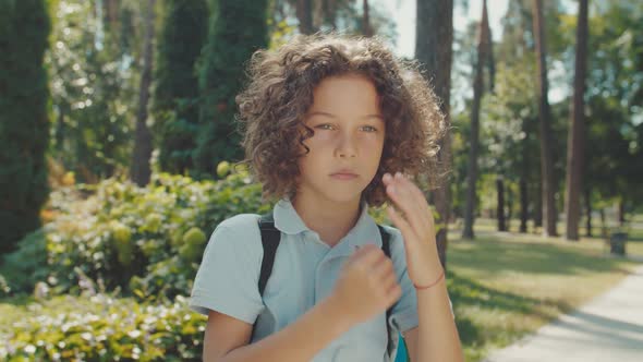 Portrait of Curly Boy with Backpack Looking Into Camera Outdoors