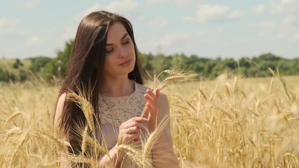 Portrait of Young Charming Woman in Dress in Wheat Field on Sunny Day Put Wheat Spike Near Her Face