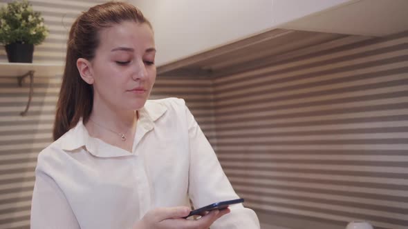 Young American Woman Is Talking on Phone While Standing in Home Kitchen