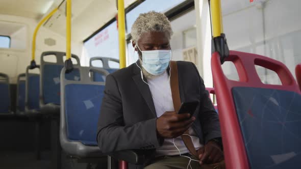 African american senior man wearing face mask using smartphone while sitting in the bus