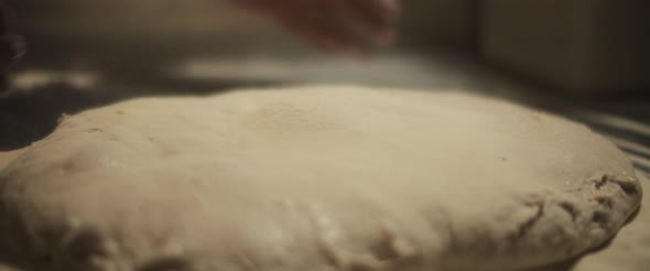 Chef spreading white flour over a fresh unprepared italian pizza dough.