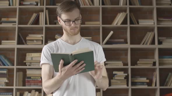 Middle Shot of Confident Caucasian Man in Eyeglasses Turning Book Page and Smiling. Portrait of