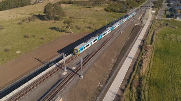 Train drives through outer suburbs aerial shot rising