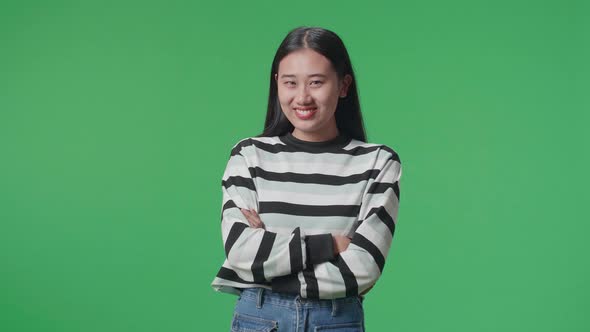 A Smiling Asian Woman Crossing Her Arms While Standing In Front Of Green Screen Background