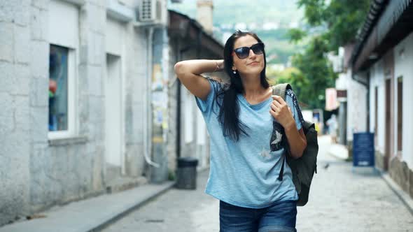 Happy Female Tourist with Backpack on Shoulders Walking Down the Street Near Vintage Buildings