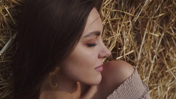 Close Portrait of Brunette Lying on a Hay Opening Eyes and Smiling Into Camera