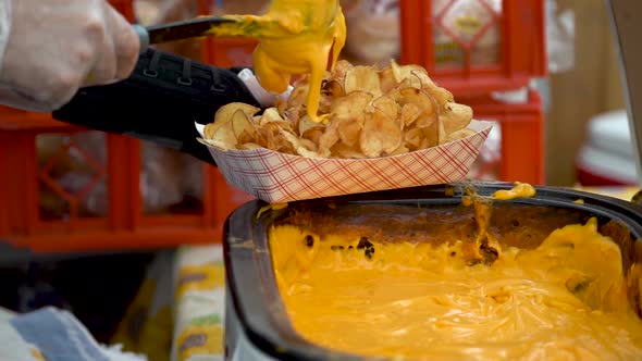 Slow motion of putting cheese sauce on a serving of tornado or curly potato fries.