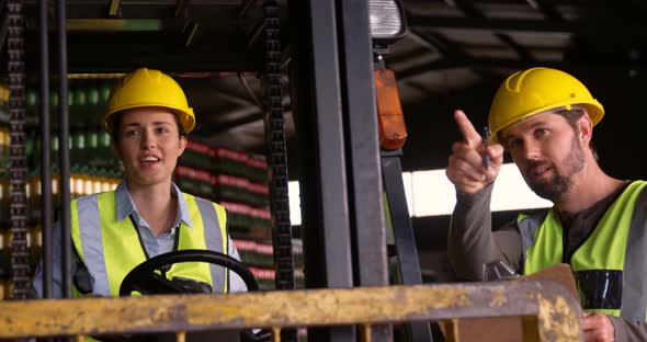 Workers sitting in forklift and talking to each other in warehouse