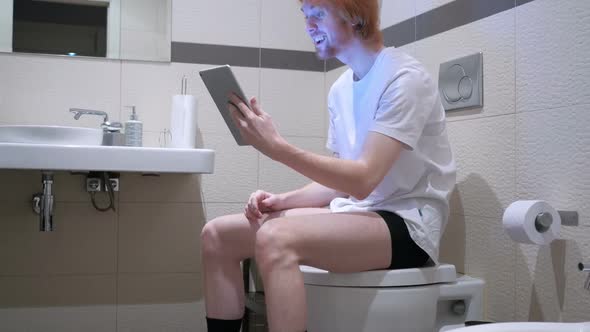 Video Chat on Tablet By Man Sitting on Bathroom Commode